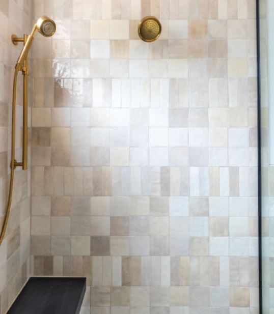 The primary bathroom shower features soft blush tiles from Bedrosians and matte gold fixtures from Kohler. Photographed by Flourish Photography